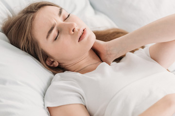Fototapeta na wymiar young woman lying in bed with closed eyes while suffering from neck pain