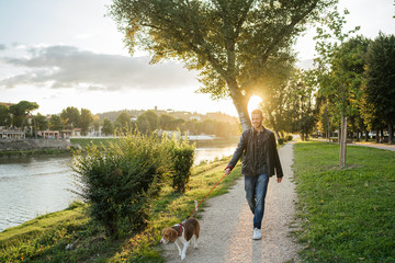 Young man takes his beloved dog for a walk in the park at sunset - Millennial in a moment of relaxation with his four-legged friend - obrazy, fototapety, plakaty