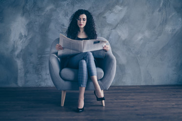 Fototapeta na wymiar Portrait of her she nice-looking attractive charming classy chic focused wavy-haired girl sitting in chair reading news paper magazine gray concrete wall background