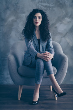 Vertical view portrait of her she nice attractive pretty classy chic content serious wavy-haired girl shark sitting in chair crossed legs job seeker attending meeting gray concrete wall background