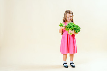 Cute little girl in a pink dress holding fresh lettuce on a light background. The concept of proper nutrition, vegetarianism. Copy space