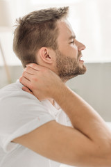 Obraz premium side view of young man touching neck while suffering from pain with closed eyes
