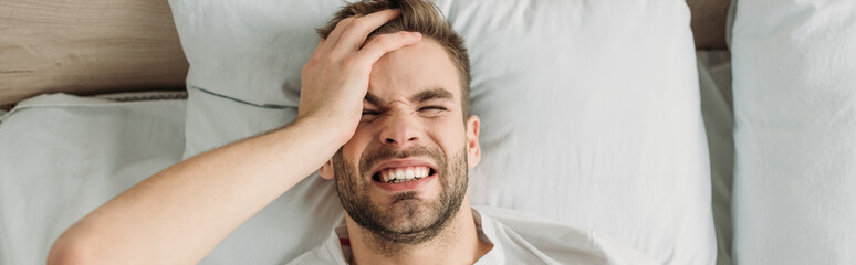 Obraz premium top view of young man touching head while suffering from migraine, panoramic shot