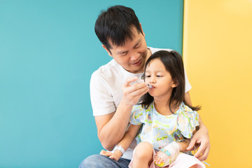 Asian father is feeding the medicine with syringe to his daughter while admit as patient in the hospital room, concept of parent care to their kid.