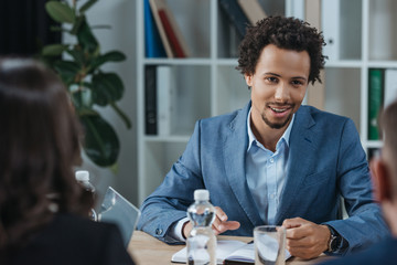 selective focus of positive african american businessman looking at colleagues at business meeting