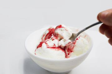 hand with spoon takes ice cream from bowl. balls of white ice cream with red berry syrup on white background