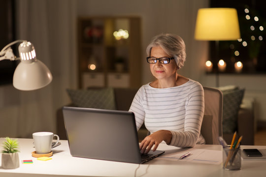 technology, old age and people concept - senior woman in glasses with laptop working at home in evening