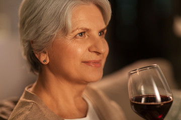 people, alcohol and drinks concept - close up of happy senior woman drinking red wine from glass at home in evening