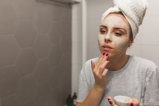 woman applying clay face mask in bathroom