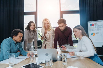 mature businesswoman looking at talking girl during business meeting with young multicultural colleagues