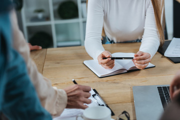 cropped view of businesswomen holding pens near notebook and clipboard at business meeting