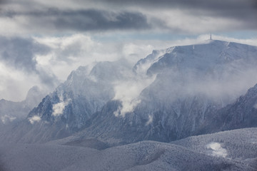 Beautiful mountain panorama in winter with fog and clouds. Bucegi mountains seen from Postavaru, Romania.