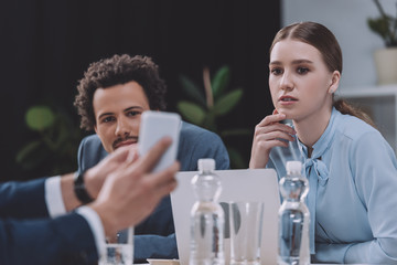 cropped view of businessman showing smartphone to multicultural colleagues