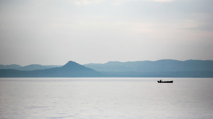 Fototapeta na wymiar Lake Garda, Italy. A view of a solitary fisherman in his boat with a backdrop of the Italian Alps.