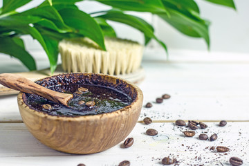 Coffee scrub in a wooden bowl with a wooden spoon on a white wooden background. Nearby is a bowl with coffee grounds, coffee grains and green flower leaves. Close-up of mine space. Coffee grounds bod