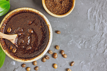 Coffee scrub in a wooden bowl with a wooden spoon on a dark stone background. Nearby is a bowl with coffee grounds, coffee grains. Coffee grounds body scrub. Close-up of mine space.