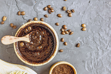 Coffee scrub in a wooden bowl with a wooden spoon on a dark stone background. Nearby is a bowl with coffee grounds, coffee grains. Coffee grounds body scrub. Close-up of mine space.