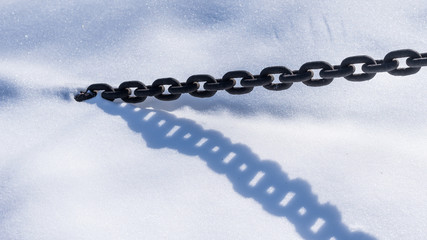 Beautiful winter background - metal chain in the snow with a shadow on a snowy surface