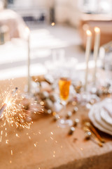 Fototapeta na wymiar New Year 2019. New Year mood. Table with a gold tablecloth, decorated with candles and tableware for celebration. Festive still life by candlelight. Bengal lights in the foreground. Close-up.