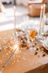 New Year 2019. New Year mood. Table with a gold tablecloth, decorated with candles and tableware for celebration. Festive still life by candlelight. Bengal lights in the foreground. Close-up.