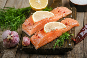 Fresh salmon steaks with herbs, lemon, rosemary and spices on a cutting board on a rustic background copy space.