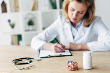 selective focus of bottle with pills, stethoscope and model of brain on wooden table