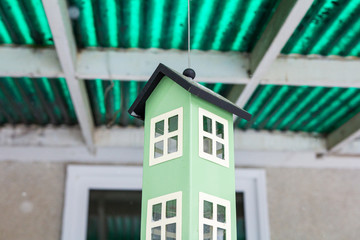 A light green bird house hangs from a green outdoor roof