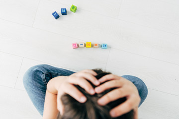 top view of sad kid with dyslexia sitting near building blocks - obrazy, fototapety, plakaty