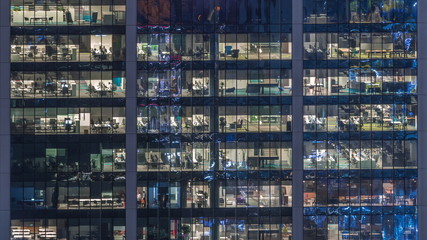 Fototapeta na wymiar Office building exterior during late evening with interior lights on and people working inside night timelapse