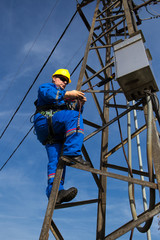 Electrician with safety belt working on electric power pole