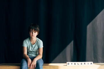 kid with dyslexia looking at camera and sitting near wooden cubes with lettering dyslexia