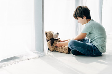 kid with dyslexia sitting on floor and looking at teddy bear