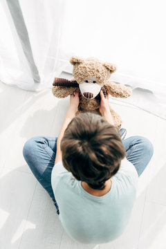 Top View Of Kid With Dyslexia Sitting On Floor And Looking At Teddy Bear