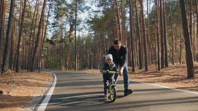 Father teaches little son to ride on the balance bike in the autumn park, happy family, slow-motion
