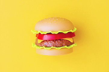 Toy burger with meat and salad on an yellow background.