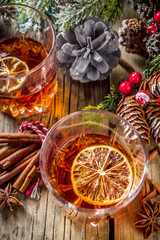 Christmas winter alcohol drink. Orange, spice and bourbon whiskey alcoholic cocktail in two glasses, wooden background with christmas tree branches and decor, copy space