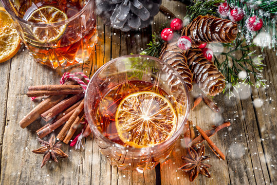 Christmas winter alcohol drink. Orange, spice and bourbon whiskey alcoholic cocktail in two glasses, wooden background with christmas tree branches and decor, copy space