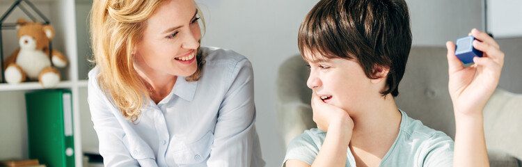 panoramic shot of smiling child psychologist looking at kid with dyslexia