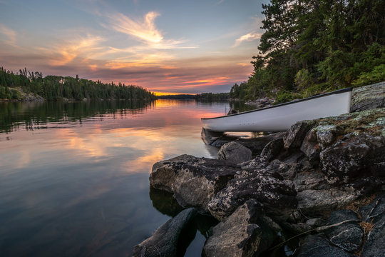 A lone canoe sits on shore on peaceful Eagle Lake at sunset. The odd colored clouds in the background are from a forest fire in Northwest Ontario, Canada in the summer of 2018.