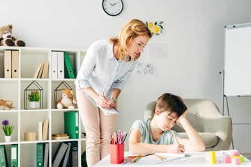 kid with dyslexia drawing with pencil and child psychologist looking at it