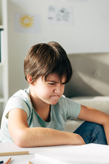 Naklejka premium irritated kid with dyslexia sitting at table and looking away