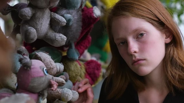 Charming sad little girl standing near shelf with toys in forest