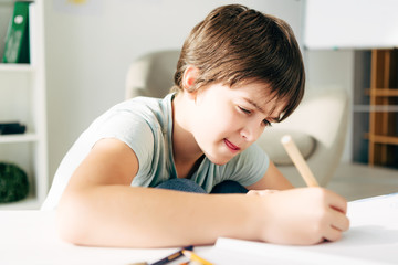 kid with dyslexia drawing with pencil and sitting at table - obrazy, fototapety, plakaty