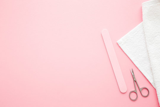 Scissors, nails file and white towel on pastel pink table. Empty place for text or logo. Closeup. Top down view.