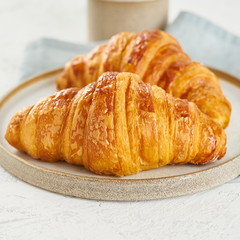 Two delicious croissants on plate and hot drink in mug. Morning French breakfast with fresh pastries. Light gray background, close up, macro