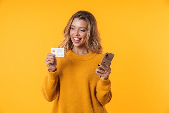 Image of pleased blonde woman holding credit card and cellphone