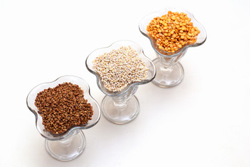 Isolated creamers with buckwheat, pearl and pea groats on white background.