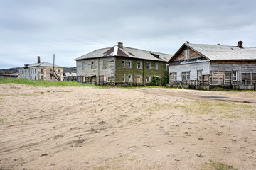 Russia, Arctic, Kola Peninsula, Barents Sea, Teriberka: Run down abandoned houses buildings in the city center of the old Russian settlement small fishing village with sandy road and grey cloudy sky.