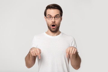 Surprised millennial guy in glasses point down demonstrating offer