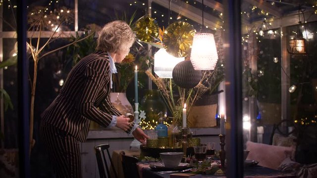 Woman preparing a decorated greenhouse in trendy christmas setting with dinner table, candles and christmas lights., 4k.